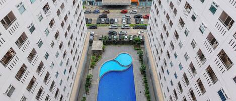 A high-rise building with a central swimming pool surrounded by greenery and a parking area.