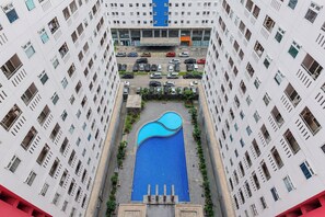 Um edifício alto com piscina central rodeada por vegetação e área de estacionamento.