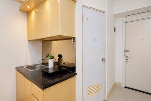 A compact kitchen with a black countertop, wooden cabinets, a sink, and a door with a lock. - Best Studio Apartment Green Pramuka City (Jakarta)