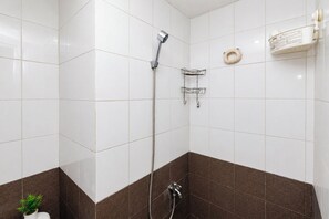 Um banheiro com azulejos brancos e marrons, chuveiro, porta-toalhas e dispensador de sabonete.