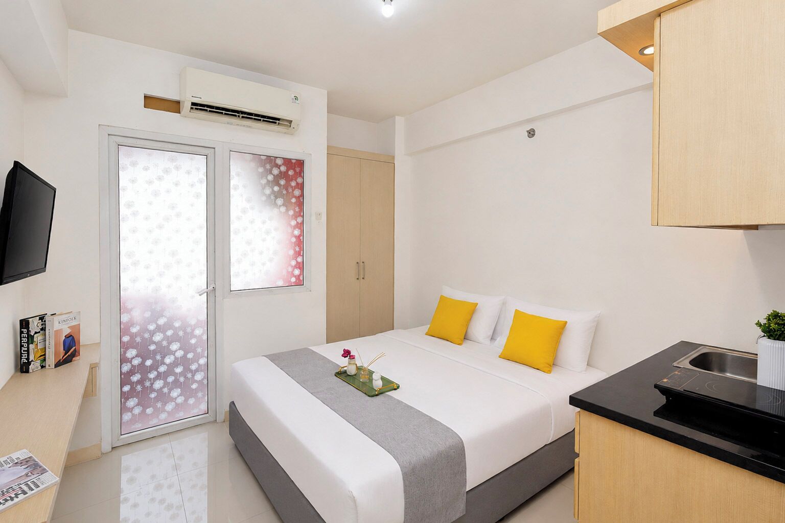 A hotel room with a bed, a desk, a television, and a kitchenette.