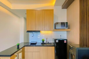 A compact kitchen with wooden cabinets, a microwave, a refrigerator, and a small sink.