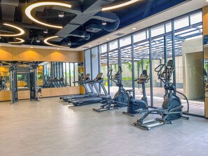 A modern gym with cardio equipment, mirrors, and a large window. - Cozy Living Studio At Apartment Saffron Noble (Bogor)