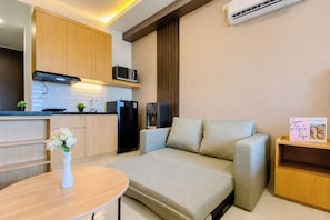 A compact living space with a kitchenette, a sofa, a small table, and a decorative item on a shelf. - Cozy Living Studio At Apartment Saffron Noble (Bogor)
