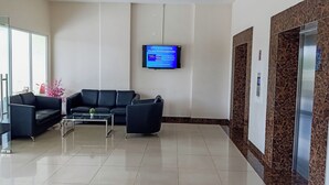 Zona de recepción con un sofá de cuero negro, una mesa de centro de vidrio y un televisor de pantalla plana montado en la pared que muestra información sobre el estacionamiento.