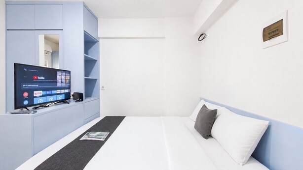 Una habitación de hotel con una cama, un televisor sobre un mueble, una estantería y un reloj de pared.