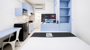 Habitación de hotel pequeña con cama, escritorio, kitchenette y televisor mostrando la interfaz de Google Play.
