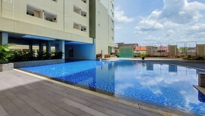 Una piscina con borde de baldosas, rodeada por un edificio con varios balcones y un cielo despejado.