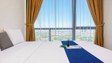 A hotel room with a large bed, a view of a cityscape through sheer curtains, and a blue accent rug.