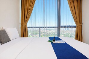 Habitación de hotel con una cama grande, vista de un paisaje urbano a través de cortinas translúcidas y un tapete azul.