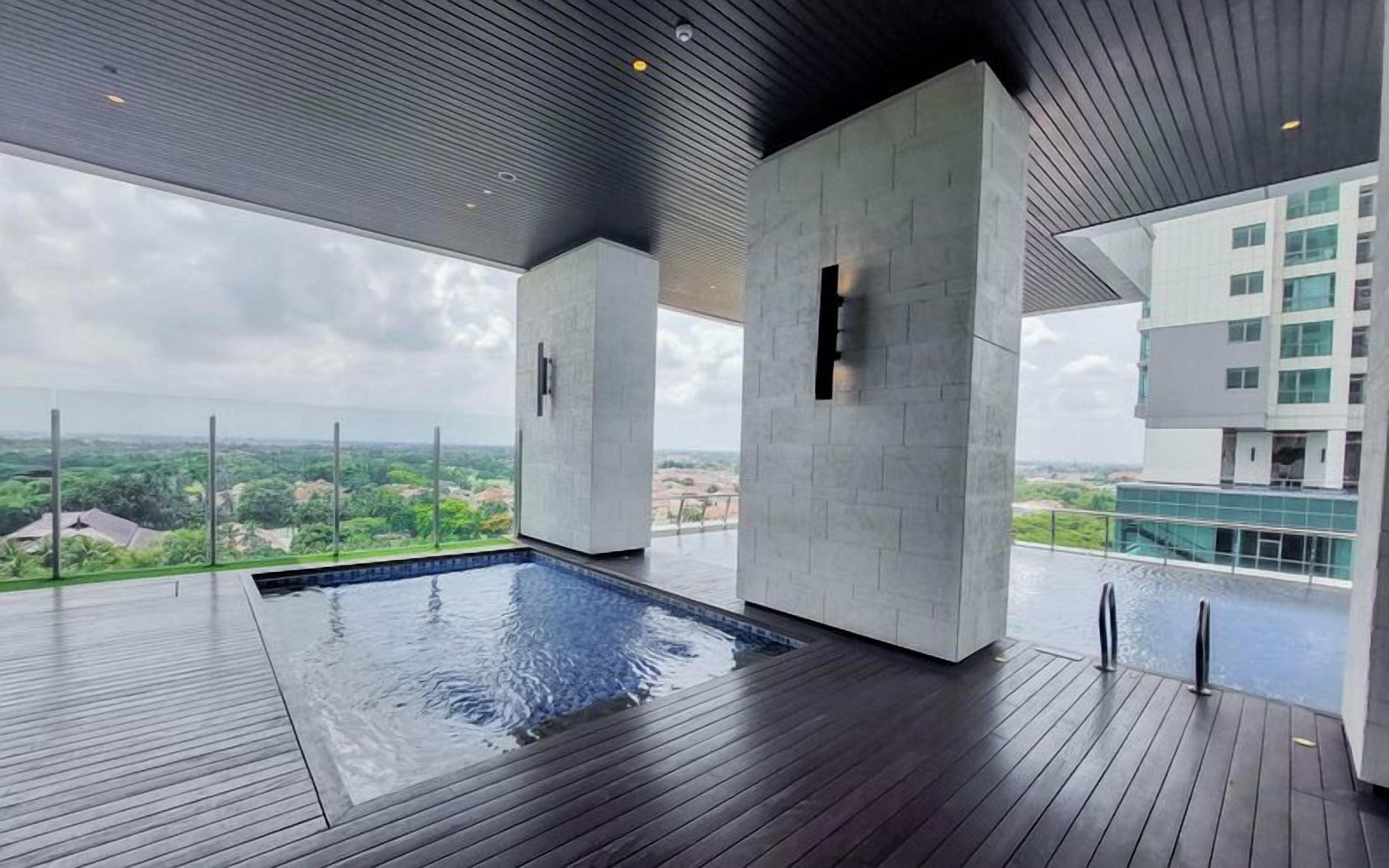 Una piscina interior moderna con un solárium de madera, pilares grandes y vistas a la ciudad.