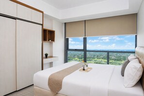 Ein modernes Schlafzimmer mit einem großen Bett, einem Kleiderschrank, einer kleinen Ablagefläche und Blick auf eine grüne Landschaft durch ein großes Fenster.
