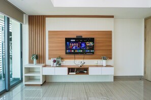 Una sala de estar moderna con un televisor de pantalla plana montado en una pared de madera, un mueble de entretenimiento blanco debajo y una puerta de vidrio que da a un balcón.