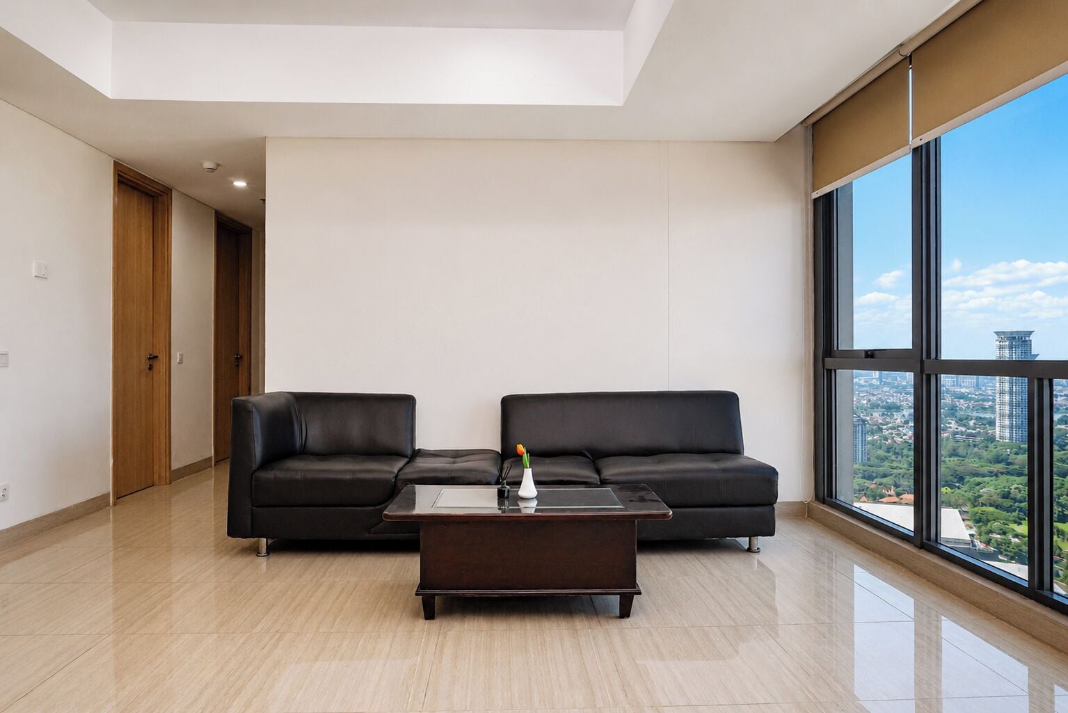 Un salon moderne avec deux canapés en cuir noir, une table basse en bois et une grande fenêtre donnant sur la ville.