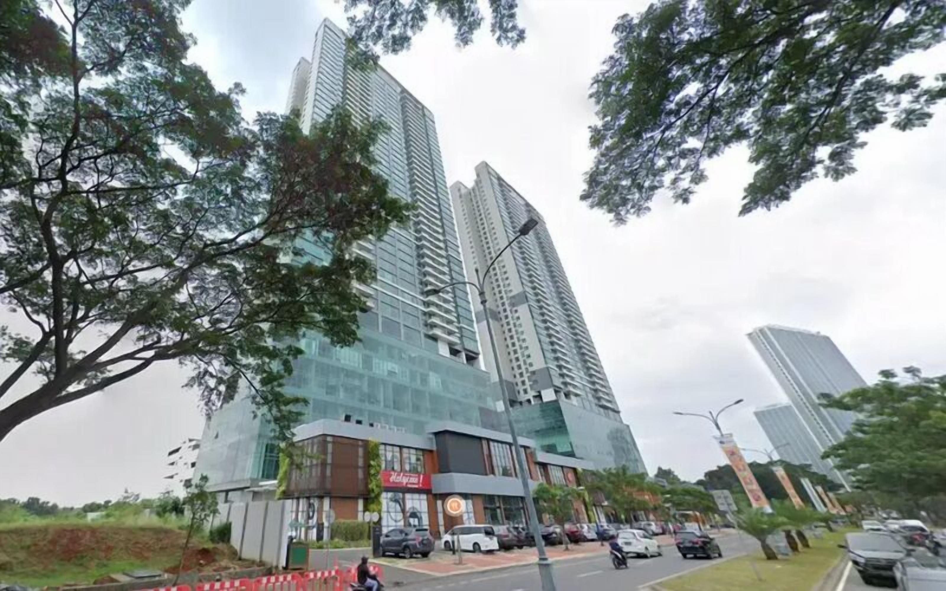 Un moderno edificio de gran altura con fachada de vidrio, rodeado de árboles y una calle con automóviles estacionados.