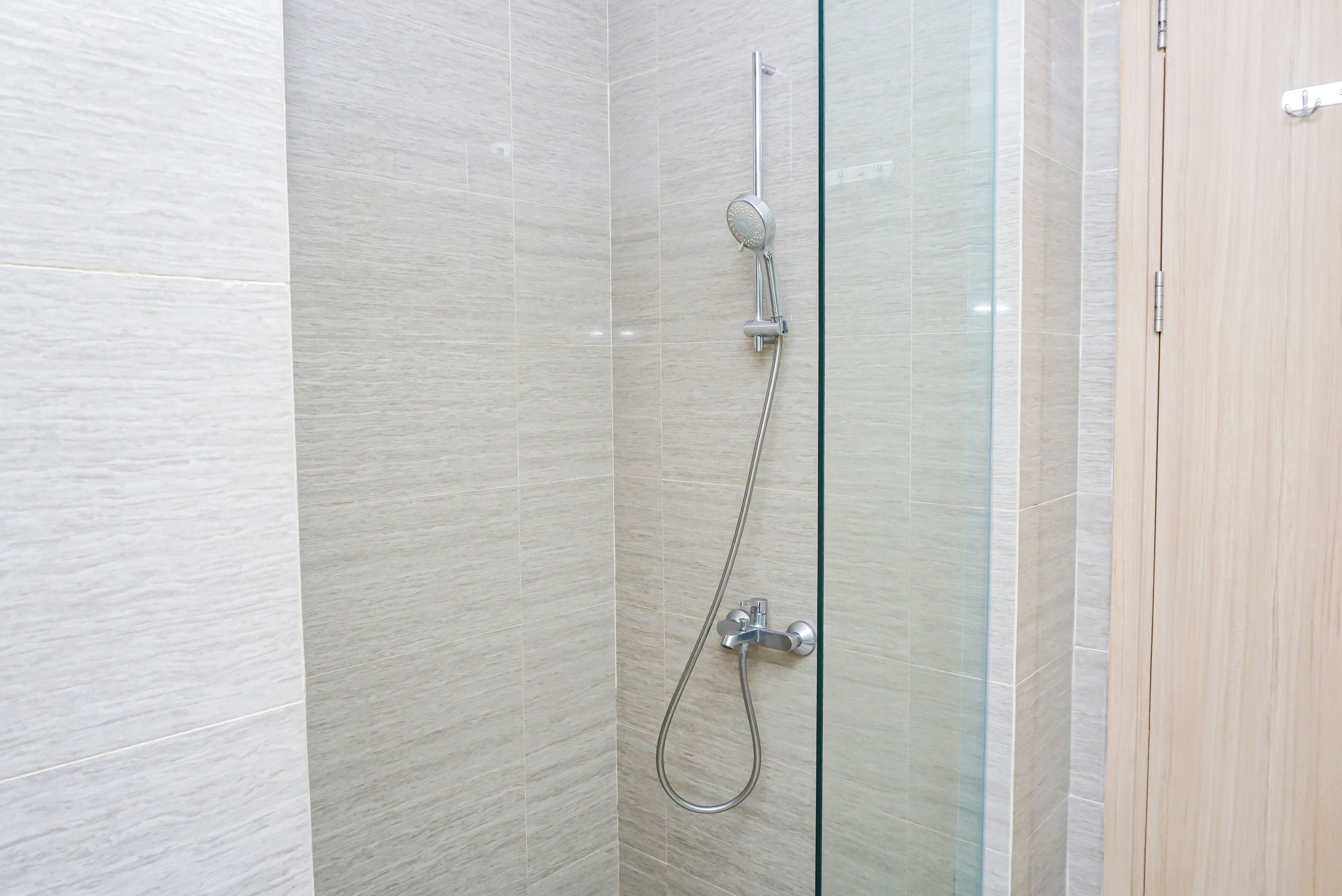 A shower with a glass door, a handheld showerhead, and a wall-mounted control panel.