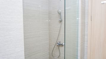 A shower with a glass door, a handheld showerhead, and a wall-mounted control panel.