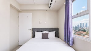 A hotel room with a bed, a window with a city view, a door, and an air conditioning unit. - Nice And Tidy 1Br At Apartment Urbantown Serpong (South Tangerang)