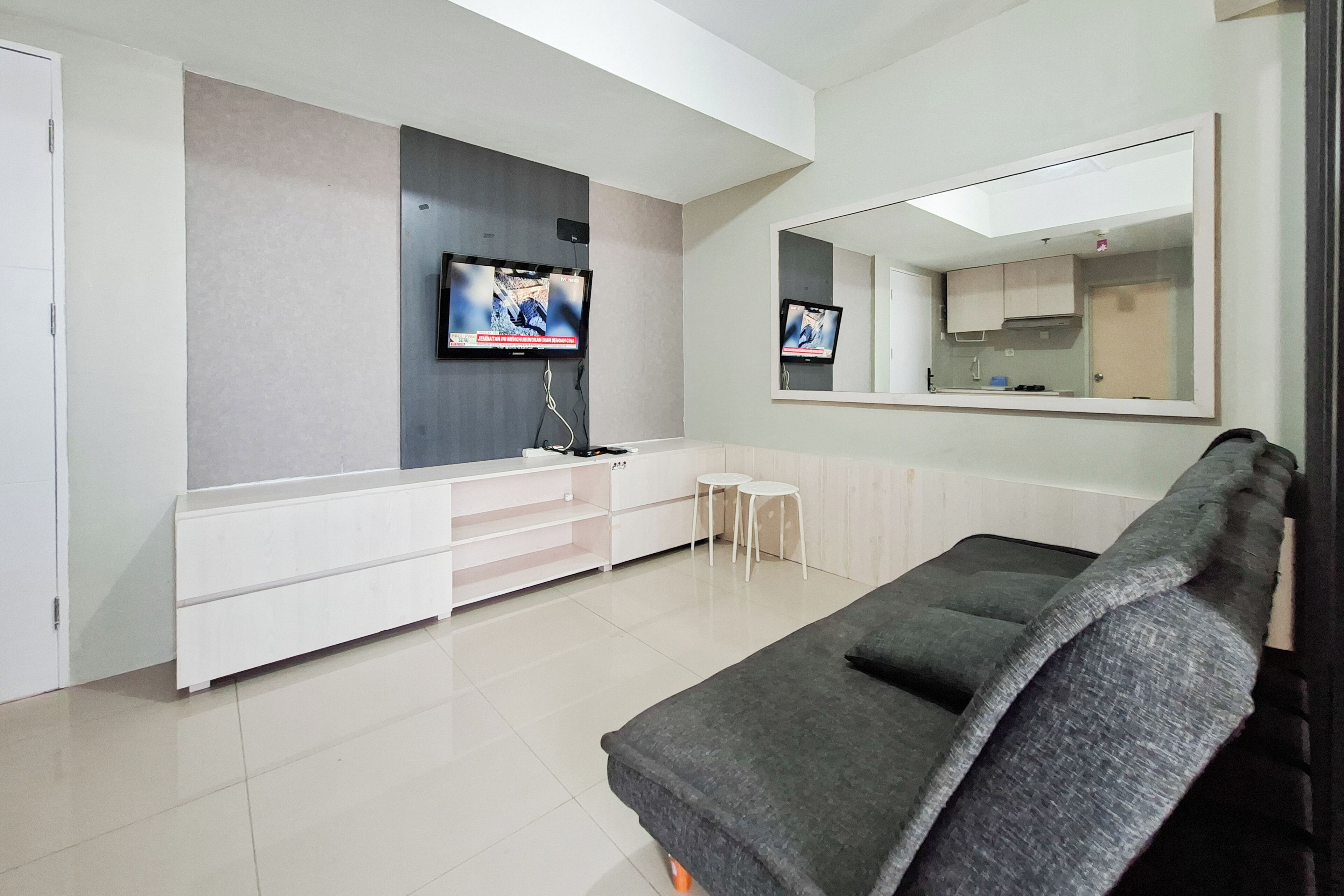 A modern living room with a grey sofa, a flat-screen TV mounted on the wall, a small white table, and a built-in cabinet.
