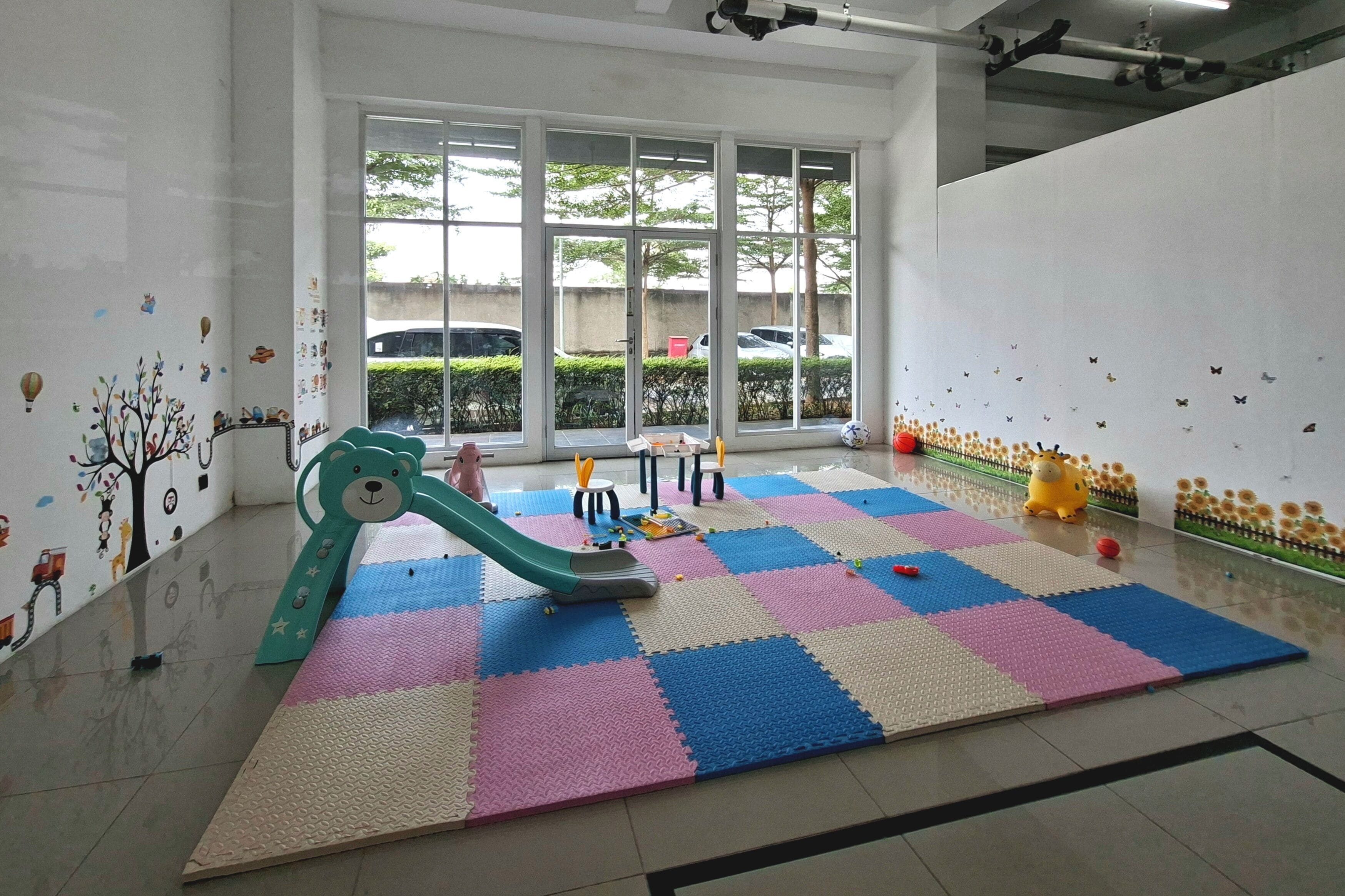A play area with a colorful interlocking floor, a green slide, and wall decorations.