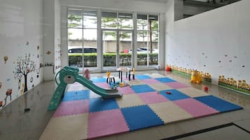 A play area with a colorful interlocking floor, a green slide, and wall decorations.