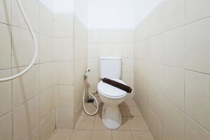 Ein kleines Badezimmer mit Fliesen, einer Toilette, einer Dusche und einem sichtbaren Rohr.