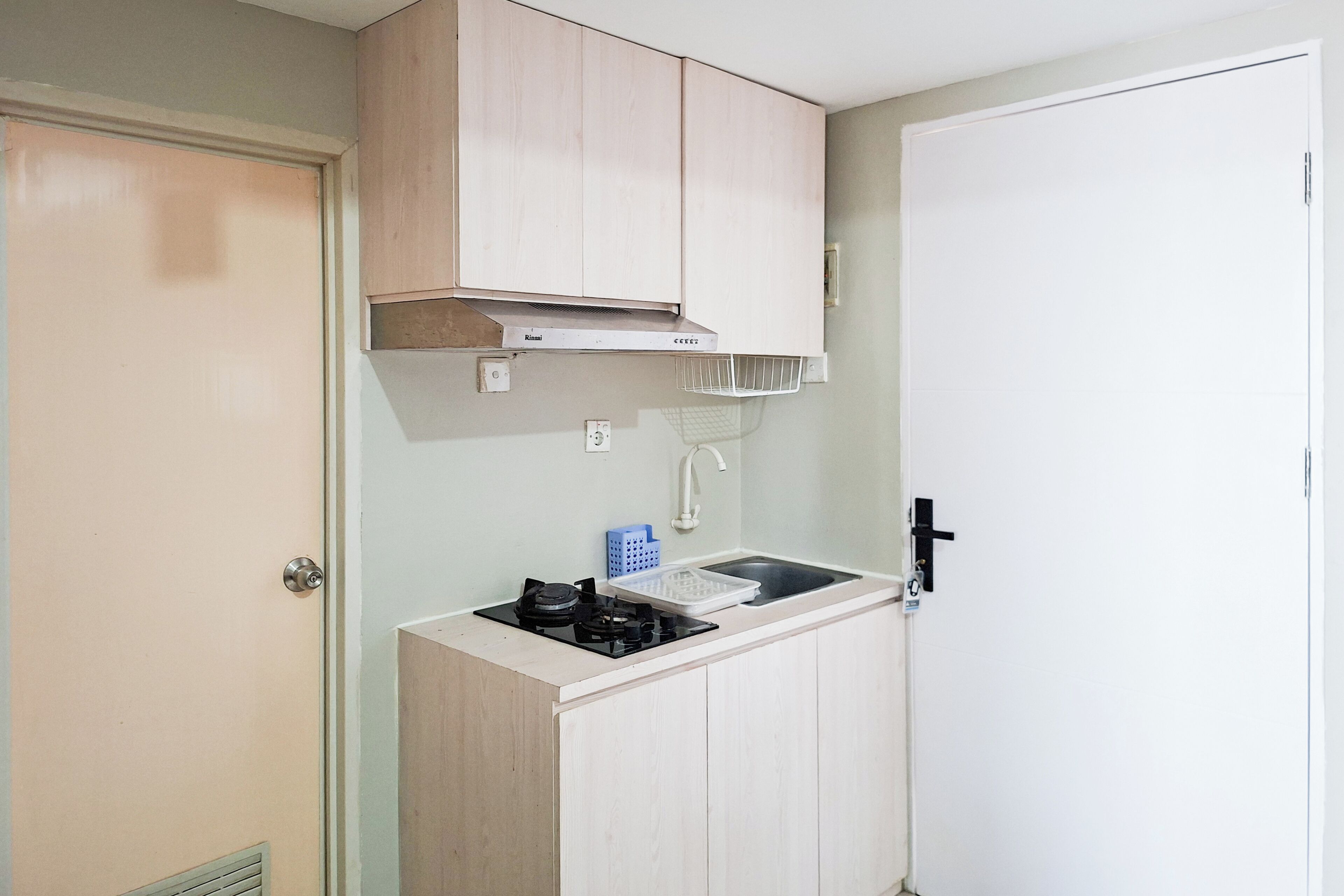 A compact kitchenette with a stove, sink, and a small cabinet above the countertop.