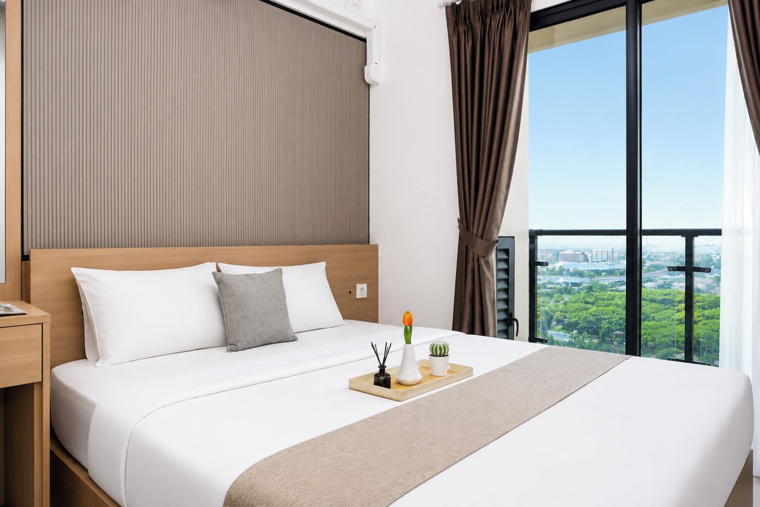 Una camera d'hotel con un letto grande, un comodino, una finestra con vista sulla città e una tenda.