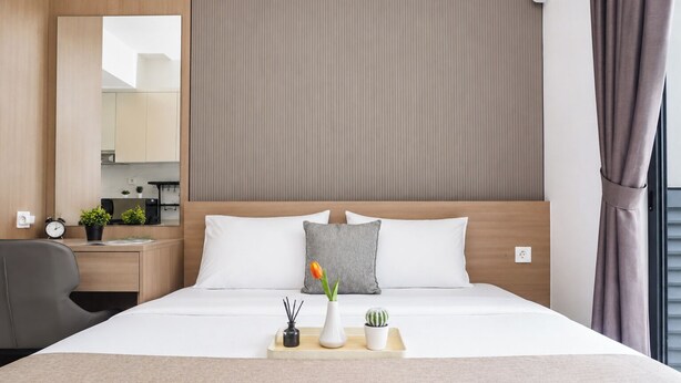 A hotel room with a bed, bedside table, chair, and a view of the outside. - Cozy Well Located Studio Room At Apartment Sky House Bsd (Tangerang)