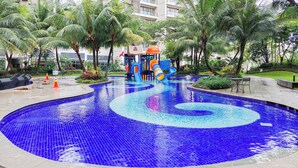 A swimming pool with a spiral design, surrounded by palm trees and a children's play area. - Cozy Well Located Studio Room At Apartment Sky House Bsd (Tangerang)