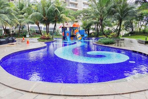 Ein Schwimmbecken mit Spiralmuster, umgeben von Palmen und einem Spielbereich für Kinder.