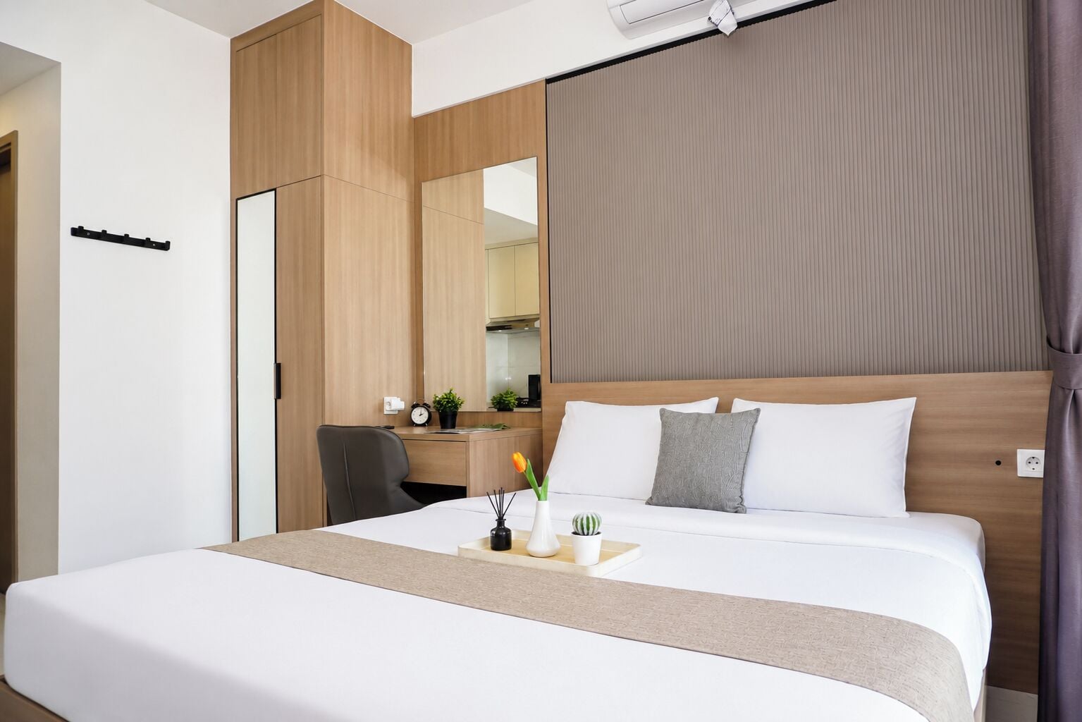 Quarto de hotel com cama, escrivaninha, cadeira e uma janela grande com cortinas.