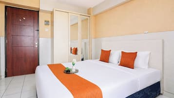 Habitación de hotel con una cama grande, una puerta de madera, un espejo y una pared blanca.