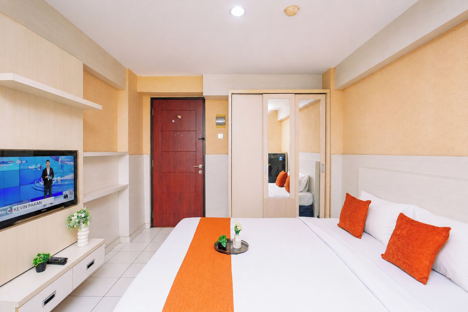 A hotel room with a bed, a TV, a door, and a mirror.