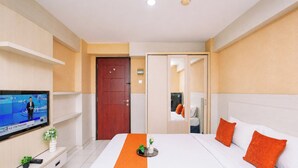 Una habitación de hotel con cama, televisor, puerta y espejo.