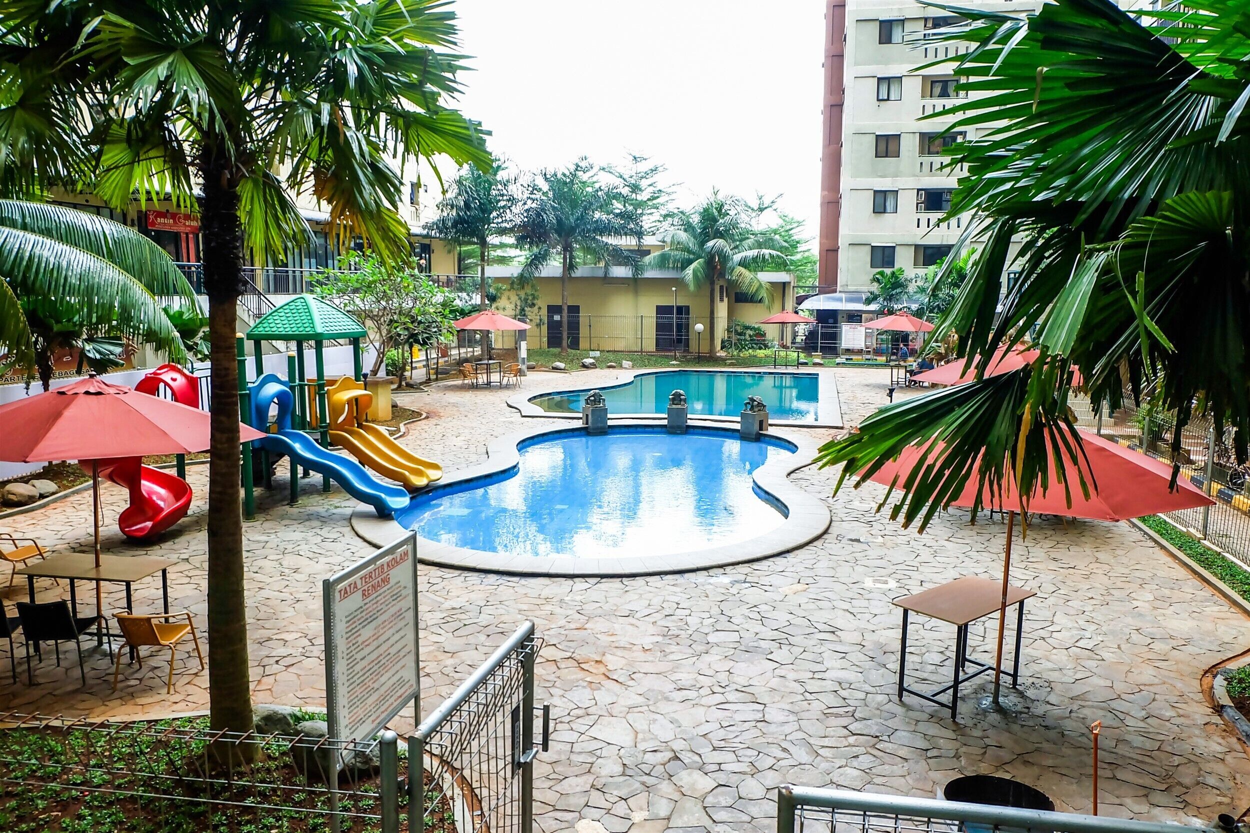 A children's play area with slides and a pool, surrounded by palm trees and outdoor seating.
