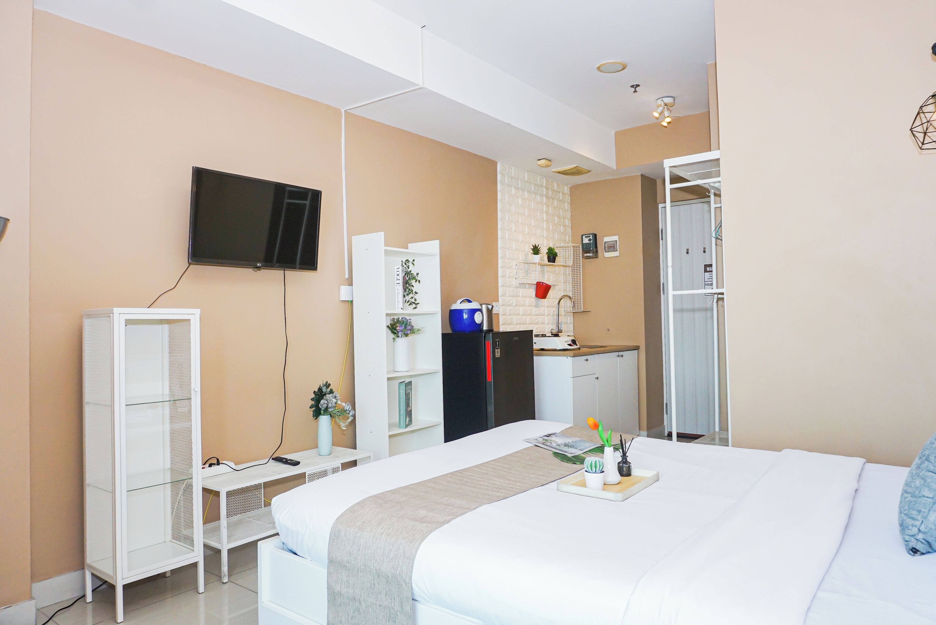 A hotel room with a bed, a TV mounted on the wall, a kitchenette, and a wardrobe.