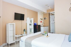 Habitación de hotel con cama, televisión montada en la pared, kitchenette y armario.