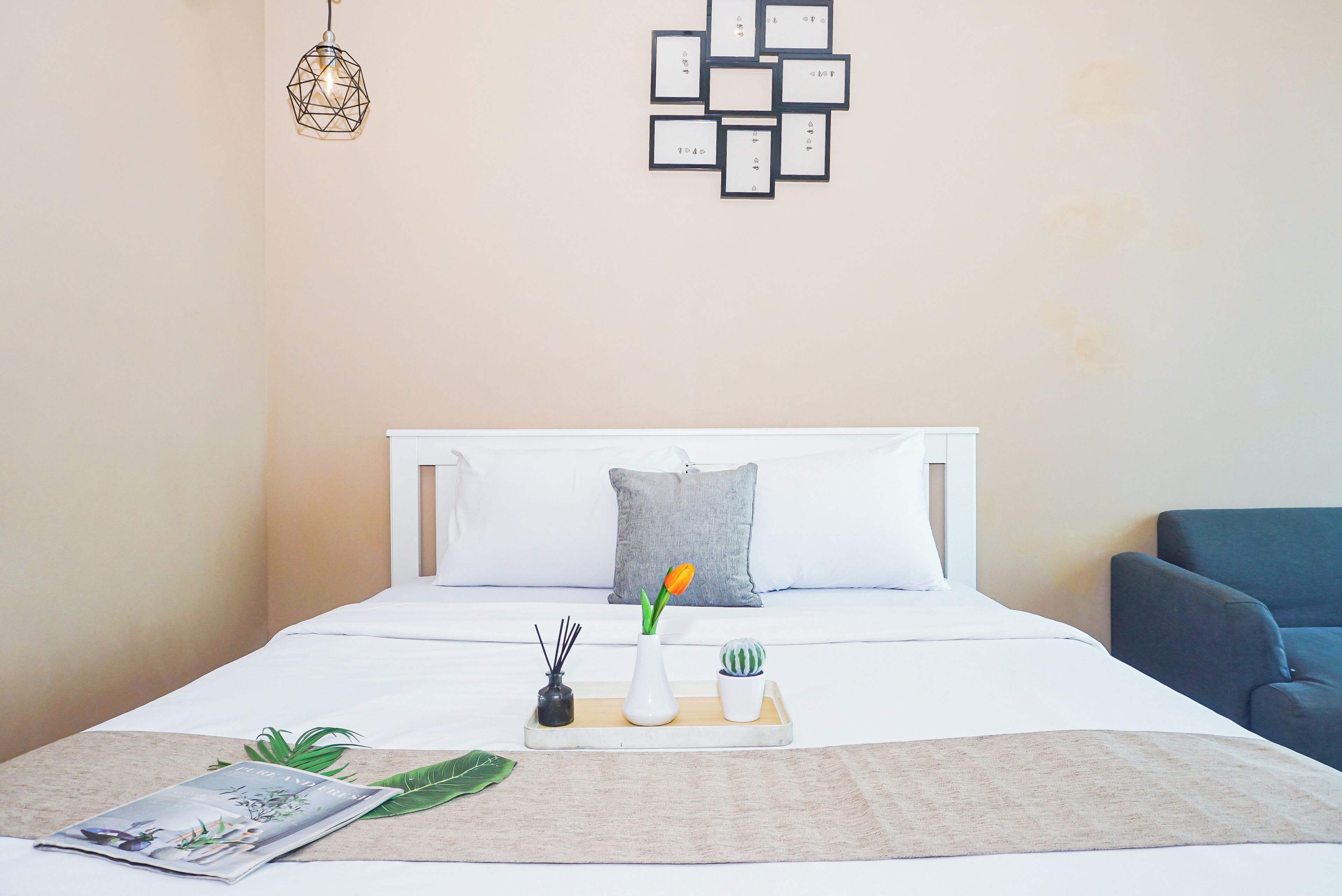 A neatly made bed with white bedding, a grey pillow, a tray with a vase, and a magazine on the side.