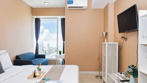 Quarto de hotel com cama, escrivaninha, cadeira, televisão, ar condicionado, janela com cortinas e vista da cidade.