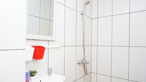 Casa de banho com paredes revestidas a azulejos brancos, uma pia branca, um cesto de lixo vermelho e um chuveiro com chuveiro manual.