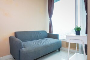 Una habitación pequeña y moderna con un sofá gris, una silla blanca, una ventana con cortinas y una planta en una mesita.