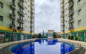 A swimming pool surrounded by high-rise residential buildings with balconies and air conditioning units. - Bright And Warm Combined 2Br At Apartment Suites @Metro (Bandung)