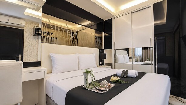 A modern hotel room with a bed, bedside table, and a large mirror. - Bright And Warm Combined 2Br At Apartment Suites @Metro (Bandung)