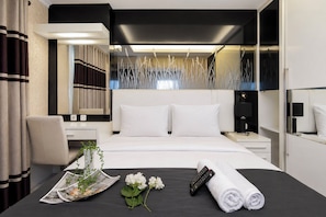 A modern hotel room with a large bed, bedside tables, a desk, and a mirror. - Bright And Warm Combined 2Br At Apartment Suites @Metro (Bandung)