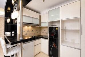 A modern kitchen with white cabinets, a black countertop, and a refrigerator with a decorative flower design. - Bright And Warm Combined 2Br At Apartment Suites @Metro (Bandung)