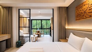 A hotel room with a large bed, a dining area, and a view of greenery through the windows. - Serene 1Br With Nature View At Apartment Lavaya Nusa Dua Bali (Bali)