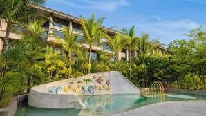 A swimming pool with a dolphin mural, surrounded by palm trees and a hotel building. - Serene 1Br With Nature View At Apartment Lavaya Nusa Dua Bali (Bali)