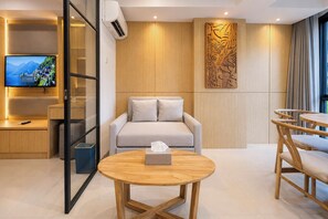 A modern hotel room with a sofa, a round wooden table, a TV, and a decorative wall panel. - Serene 1BR Lavaya Nusa Dua Bali (Bali)