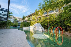 A swimming pool with a slide, surrounded by lush greenery and modern buildings. - Serene 1BR Lavaya Nusa Dua Bali (Bali)